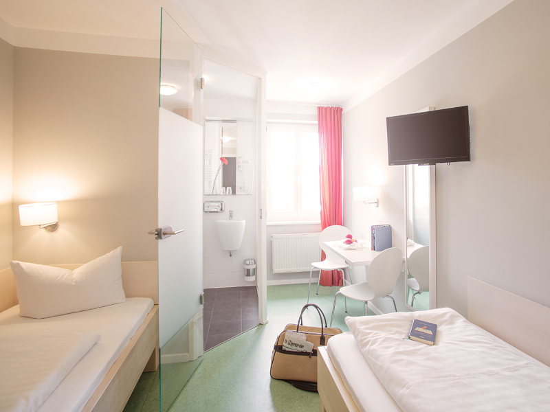Zwei getrennte Betten, Fenster und Schreibbereich im AMATO Zweibettzimmer